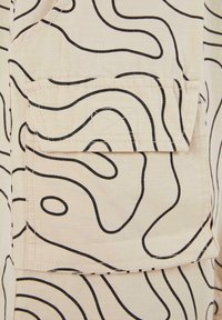 Beige fabric with a grid texture features black abstract line patterns. Includes a patch pocket with a flap at the top.