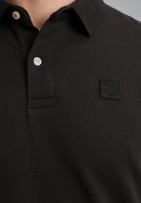 Zwarte poloshirt van een soepel katoenmix, met een twee-knopenknopsluiting en een gestructureerde borstpatch met logo-detail.