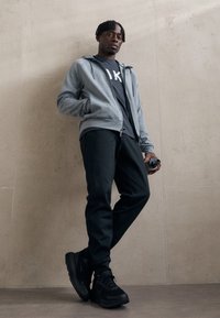 Gray zip-up hoodie over a black t-shirt, paired with black joggers and sneakers. Smooth fabric, athletic fit, and minimalistic design details.