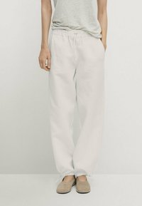 Lichte, loszittende, witte broek met een elastische tailleband en trekkoord. In combinatie met beige schoenen, voor een ontspannen uitstraling.