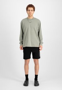 Olkiharmaa pitkähihaisen paidan yhdistelmä mustien shortsiin, mustat sukat ja mustat slip-on kengät. Yksinkertainen, rento muotoilu ilman kuvioita.