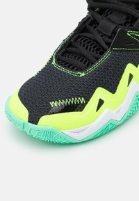 Czarny but sportowy z neonowozielonymi akcentami, teksturowaną cholewką, zygzakowatym wzorem oraz miętowozieloną podeszwą z wyraźnym bieżnikiem.