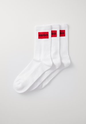 Weiße Baumwollsocken mit gerippter Textur, featuring rote rechteckige Akzente mit dem schwarzen Text "HUGO" an den Bündchen. Drei Paare enthalten.