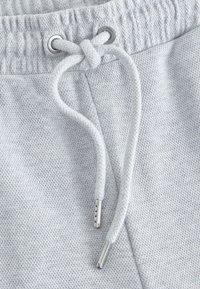 Light gray sweatpants with a textured fabric, featuring a knotted drawstring threaded through silver eyelets and metal tips.
