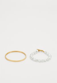 Gold metal bangle next to a bracelet made of irregular white pearls, featuring a gold toggle clasp. Both accessories have a smooth finish.