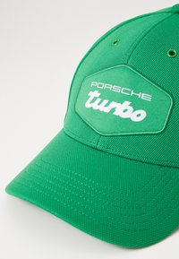 Cappellino da baseball verde con tessuto testurizzato, visiera arrotondata e una toppa esagonale con la scritta "Porsche turbo" in lettere bianche.