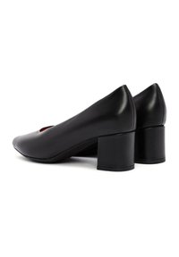 Décolleté nere in pelle con tacco a blocco, dalla punta affusolata e dettagli intagliati, caratterizzate da una texture liscia e un design minimale.