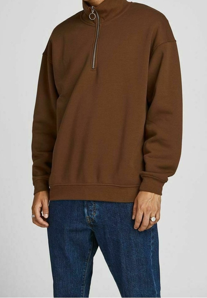 Sudadera marrón con cremallera y alto cuello, con puños acanalados, combinada con pantalones vaqueros azul denim. La tela parece suave y ligeramente texturizada.