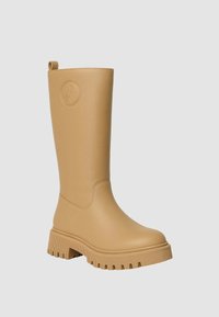 Stivali alti fino al ginocchio in gomma color sabbia, con punta arrotondata, suola spessa scanalata e logo impresso sul lato esterno. Finitura liscia opaca.