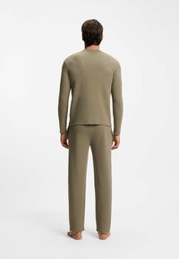 Oliivinvihreä puuvillasta valmistettu kahden osan pyjama, jossa on pitkähihainen paita pyöreällä kaula-aukolla ja siihen sopivat löysät housut. Teksturoidut kankaat.
