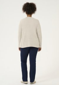 Cardigan tricot léger gris clair avec une coupe décontractée, des manches longues et un ourlet droit, porté par-dessus un jean bleu foncé et des chaussures claires.