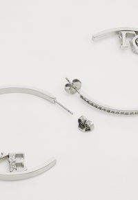 Boucles d'oreilles en argent avec un design incurvé, l'une d'elles présente un accent floral. L'autre pièce a une rangée de gemmes claires attachées.