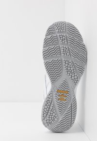 Hvid sneakersål med gummimateriale, teksturerede mønstre og zigzag-riller. Brandlogo og synlige etiketter med "olieafvisende, skridsikre".