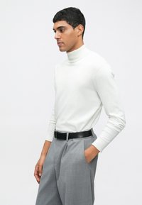 Suéter branco de gola alta feito de material macio com mangas longas, combinado com calças cinza claro e um cinto preto. Design simples, forma ajustada.