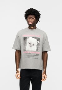 Γκρι κοντομάνικη μπλούζα με ζωγραφιστό λευκό γατάκι και ροζ κείμενο που αναφέρει ελλιπείς λεπτομέρειες για γάτα και προσφορά ανταμοιβής.