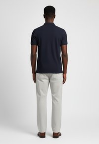 Námořnické polo tričko z texturované látky, spárované se světle šedými kalhotami. Oba kousky mají přiléhavý střih a minimalistický design.
