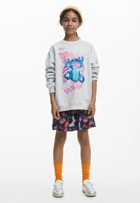Grå sweatshirt med en färgglad Stitch-grafik, i kombination med en svart kjol som visar livliga matteman, orange knästrumpor och silverfärgade skor.