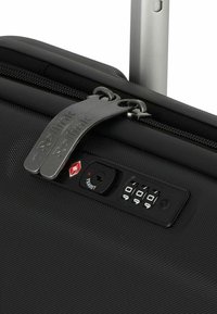 Valise rigide noire avec une surface texturée, double fermetures éclair en métal, un cadenas à combinaison TSA et une poignée rétractable.
