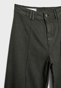 Jeans verde scuro con taglio dritto, realizzati in denim texturizzato. Presentano un bottone metallico, chiusura con zip frontale e cuciture doppie. Etichetta della taglia visibile.