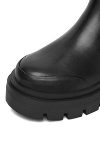 Melni ādas potītes zābaki ar noapaļotu purngalu, biezu platformu un teksturētu apdari. Šuvju detaļas izceļ dizainu.