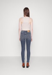 Ljust beige ribbad ärmeless top som kombineras med mörkblå tajta jeans med bakfickor och ett brunt läderpatch vid midjan.