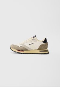 Beige og lysebrune sneakers med semsket materiale, mesh-detaljer, forsterket hæl og en teksturert svart gummisåle. Har en diskret logo.