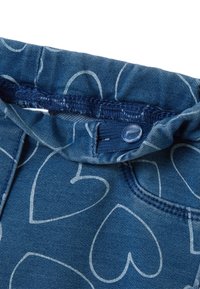 Tela de mezclilla azul con un patrón de corazones en gris claro. Presenta una cinturilla elástica y un detalle de botón de plástico azul.