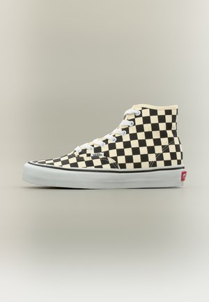 Ανδρικά παπούτσια Vans με ψηλό κολάρο σε ασπρόμαυρο σχέδιο με μοτίβο σκακιέρας, άσπρα κορδόνια και χοντρή λευκή σόλα με κόκκινο λογότυπο Vans στη φτέρνα.