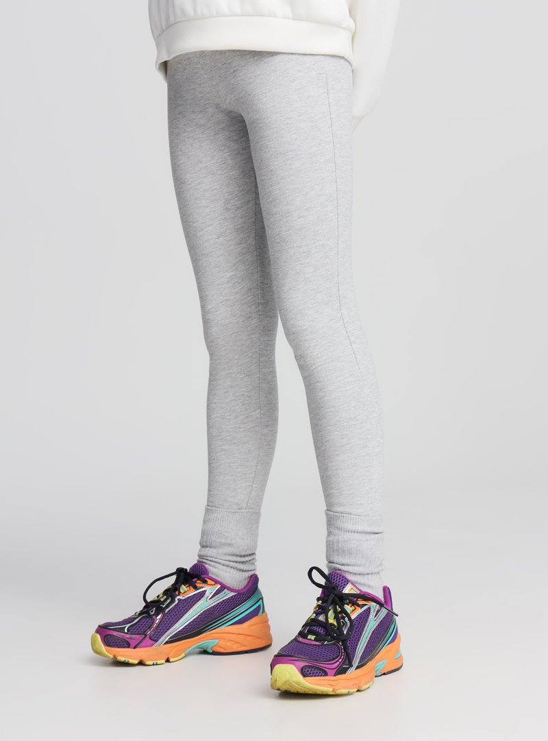 Leggings grigio chiaro con una texture liscia, dalla vestibilità aderente. Abbinati a sneakers multicolori con accenti viola, turchese e arancione.