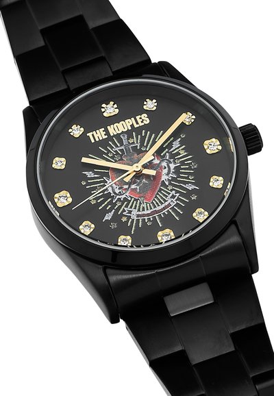 El reloj analógico negro presenta una correa texturizada negra, una esfera negra con un diseño gráfico, acentos dorados y marcadores de hora de cristal.
