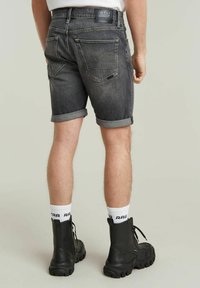 Zwarte denimshorts met opgerolde zomen, voorzien van zakken en een label op de tailleband. Gecomplementeerd met zwarte laarzen en witte sokken met logo.