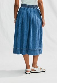 Denim midi sukně se smockovaným pasem, sklady, lem s kontrastním šitím, spárovaná s bílými sandály na řemínky.