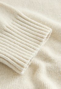 Close-up van crèmekleurige gebreide stof met een geribbelde manchetkant, met details van de textuur en steken op zacht wollen materiaal.