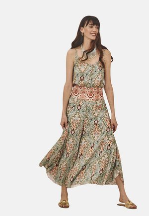 Vestido maxi con un patrón floral en verde, rosa y crema; corpete con volantes, cintura ceñida, falda fluida. Combinado con sandalias doradas y un collar.