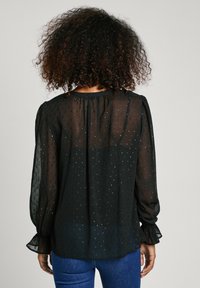 Blusa nera trasparente con maniche a sbuffo lunghe, texture a pois discreta e polsini arricciati; presenta un collo rotondo e una vestibilità ampia.