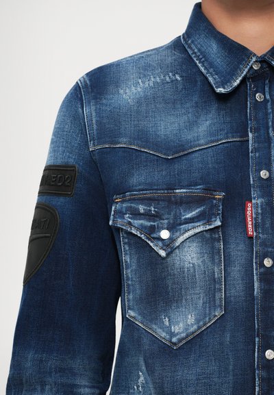 Jeansjacke mit verwaschenen Details, Druckknopf-Taschenklappe, schwarzen Patches an den Ärmeln und rotem DSQUARED2-Label an der Naht der Brusttasche.