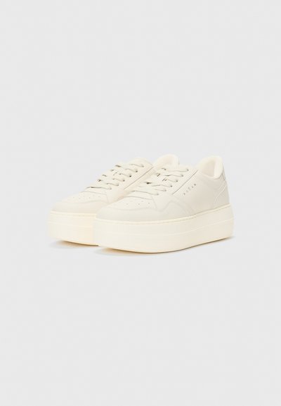 Baskets ivoire avec une finition en cuir lisse, présentant un bout arrondi, des lacets plats et une semelle épaisse. Design minimaliste avec un branding subtil.
