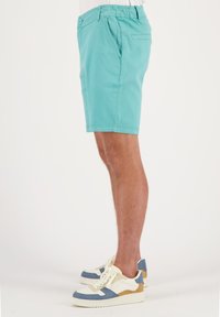 Pantalones cortos turquesa con cintura ajustable, dos bolsillos laterales y un bolsillo trasero, combinados con zapatillas blancas y azules con detalles en color marrón.