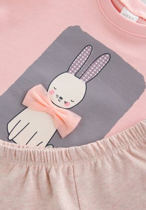 Sweat-shirt rose clair avec un motif de lapin aux oreilles à carreaux et un nœud rose, assorti à un pantalon rose à taille élastique.