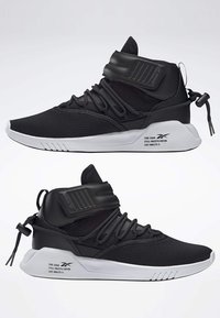 Svarta sportskor med överdel i mesh, justerbart ankelsnöre, strukturerat snörningssystem och vit gummisula.