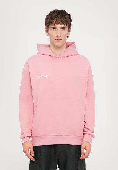 Haut à capuche rose clair en tissu doux, doté d'une poche kangourou, d'une capuche avec cordon de serrage et d'un petit détail en texte blanc sur la poitrine.