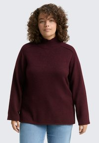 Pull à col roulé bordeaux en tricot doux, avec des manches amples et un ourlet droit, associé à un jean bleu clair.