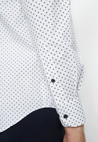 Langärmliges Hemd in Weiß und Marineblau mit geometrischem Muster, mit einem knöpfbaren Bündchen und einer glatten, leichten Stofftextur.