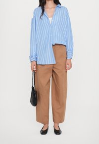 Błękitna koszula w paski z guzikami o oversize'owym kroju, beżowe szerokie spodnie, czarne baleriny i mała pleciona czarna torebka.