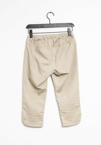 Pantalons en coton beige avec une taille élastique, longueur cropée et détails cousus. Accrochés à un cintre en plastique noir sur fond blanc.