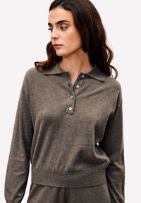 Pull-over en maille gris foncé avec col, manches longues et patte de boutonnage à quatre boutons. Texture douce avec une taille ajustée et un subtil éclat.