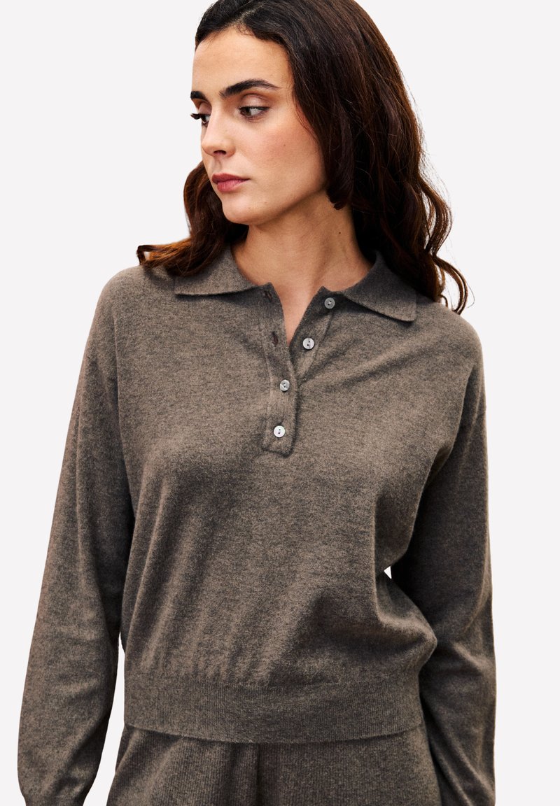 Pull-over en maille gris foncé avec col, manches longues et patte de boutonnage à quatre boutons. Texture douce avec une taille ajustée et un subtil éclat.