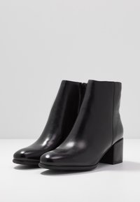 Botines de cuero negro con acabado suave, punta redondeada y tacón cuadrado de altura media. Presentan una cremallera lateral para facilitar su uso.