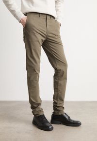Kaki bomullsbukser med slim fit og sidelommer, parret med svarte lær-sko med glatt tekstur og rund tå.
