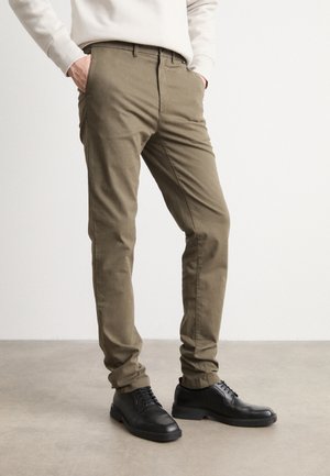 Khaki cotton trousers with a slim fit and side pockets, paired with black leather shoes featuring a smooth texture and round toe.